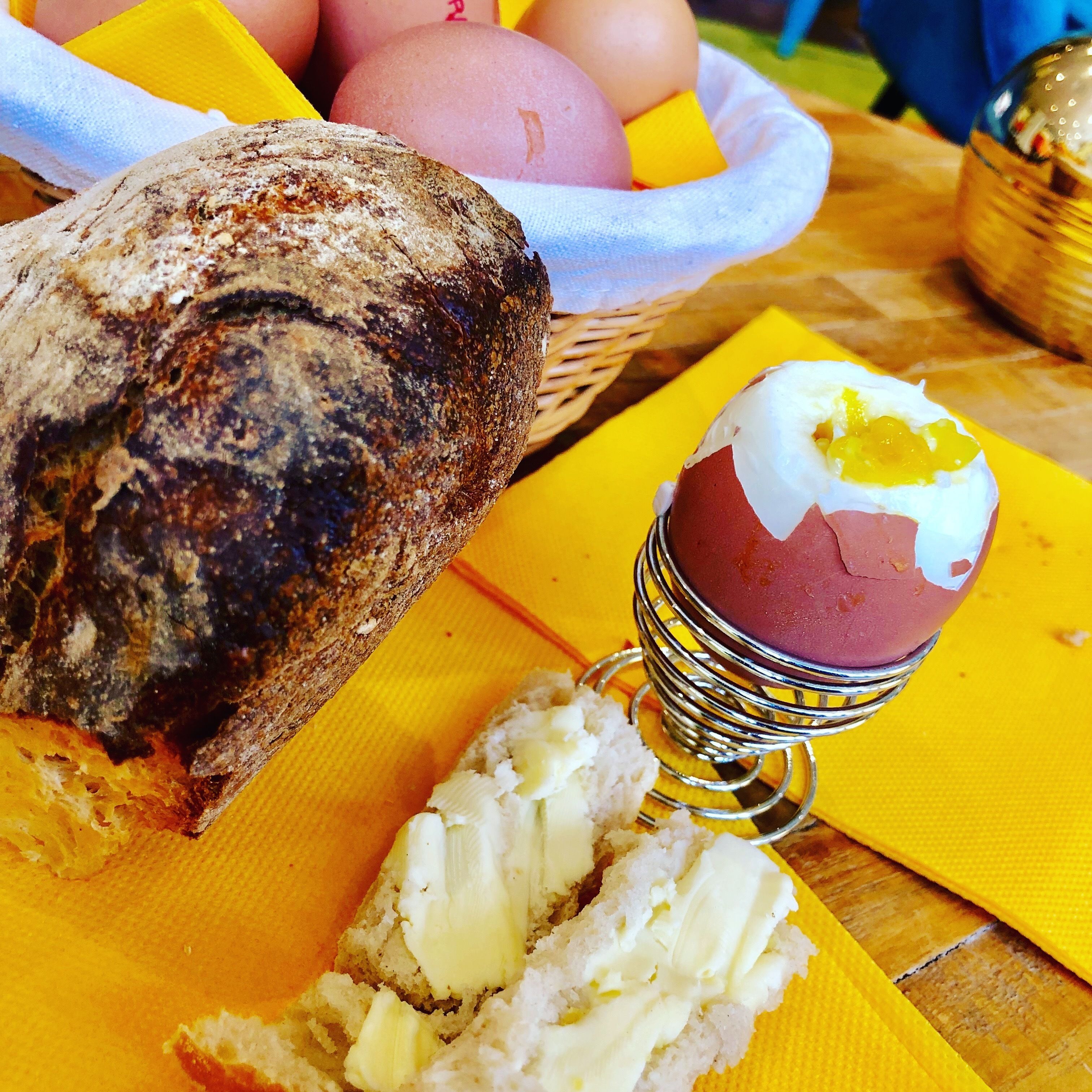 Una rebanada de pan con mantequilla, una porción de fruta con mermelada y una cesta de huevos sobre un mantel amarillo.