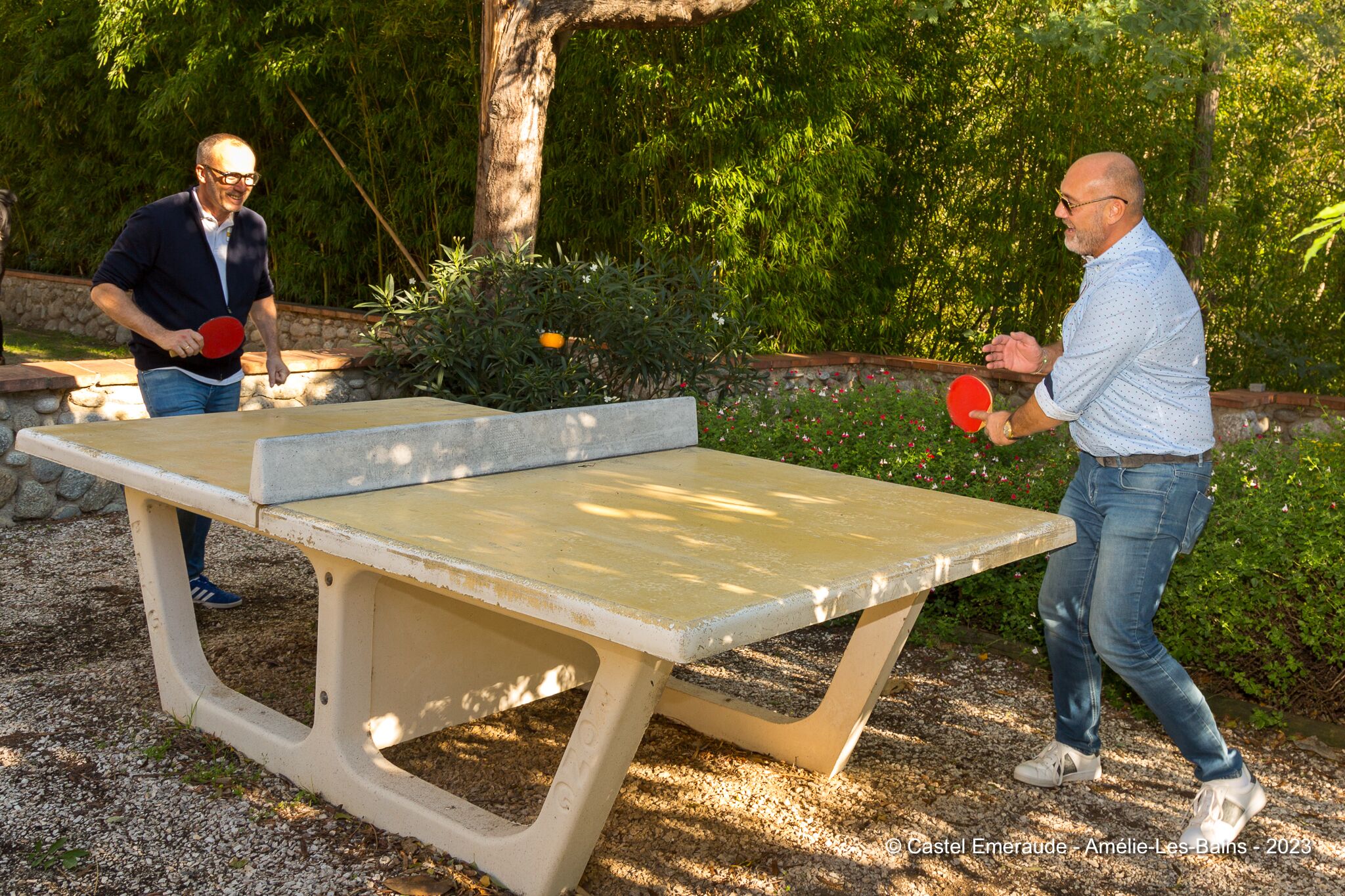 Due persone giocano a ping pong all'aperto, con tavolo e panche.