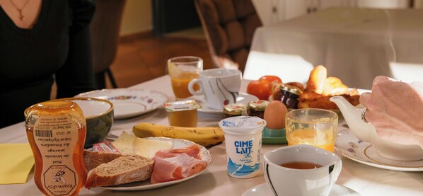 Una mesa de desayuno con diversos alimentos, una botella de miel, un vaso de jugo y un hervidor de agua.