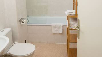 A bathroom with a toilet, a glass-enclosed shower, and a wooden shelf with towels.