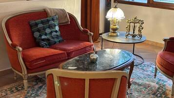 Un canapé rouge agrémenté d’un coussin à motifs, une petite table ronde avec une lampe et une chaise recouverte d’un tapis à motifs.