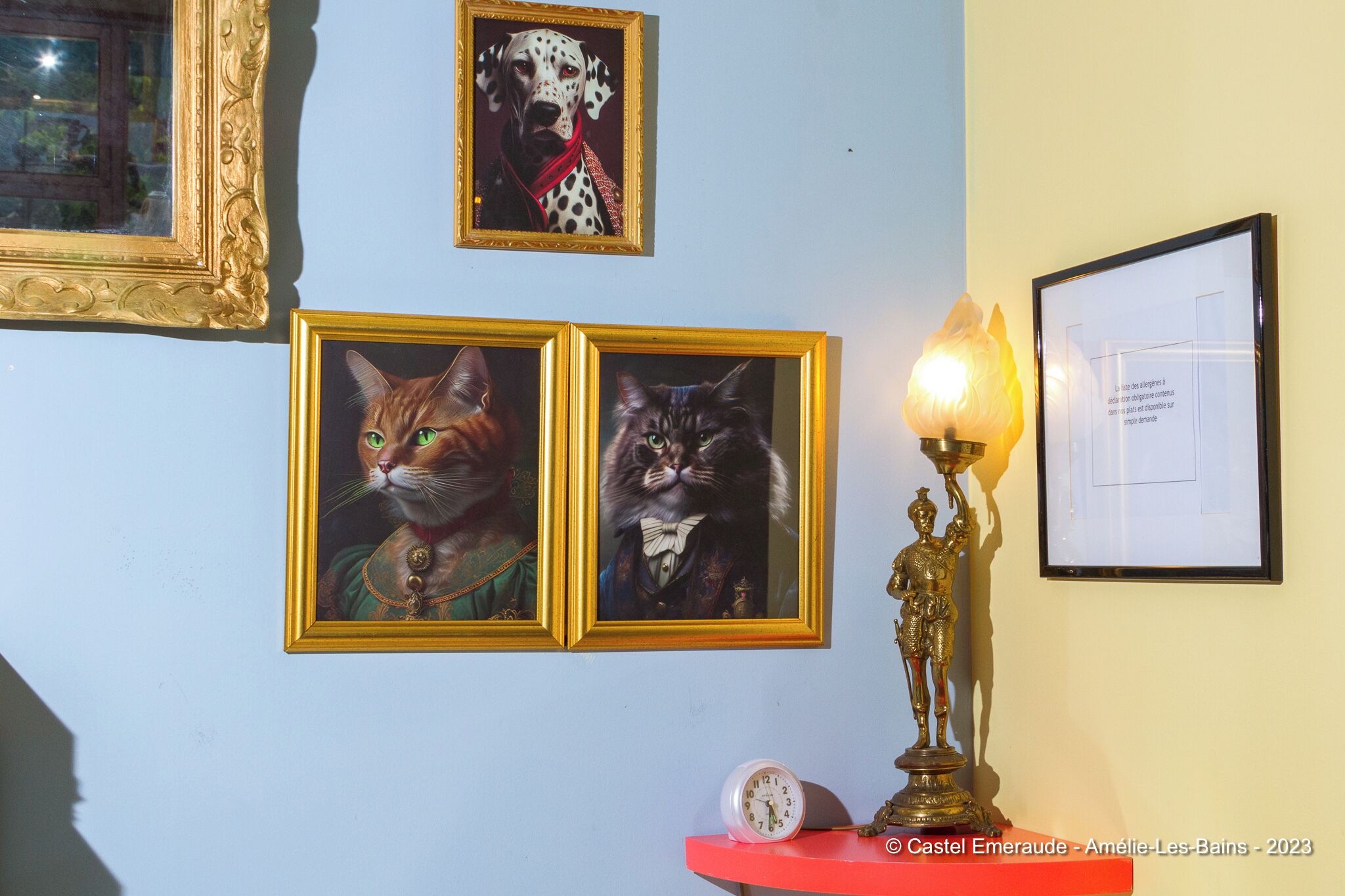 A wall with framed pictures of cats and a statue.