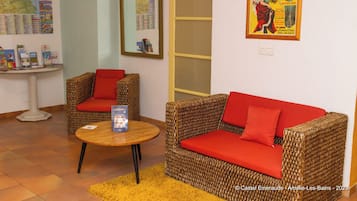 A room with wicker furniture, red cushions, a round wooden table, and a map on the wall.