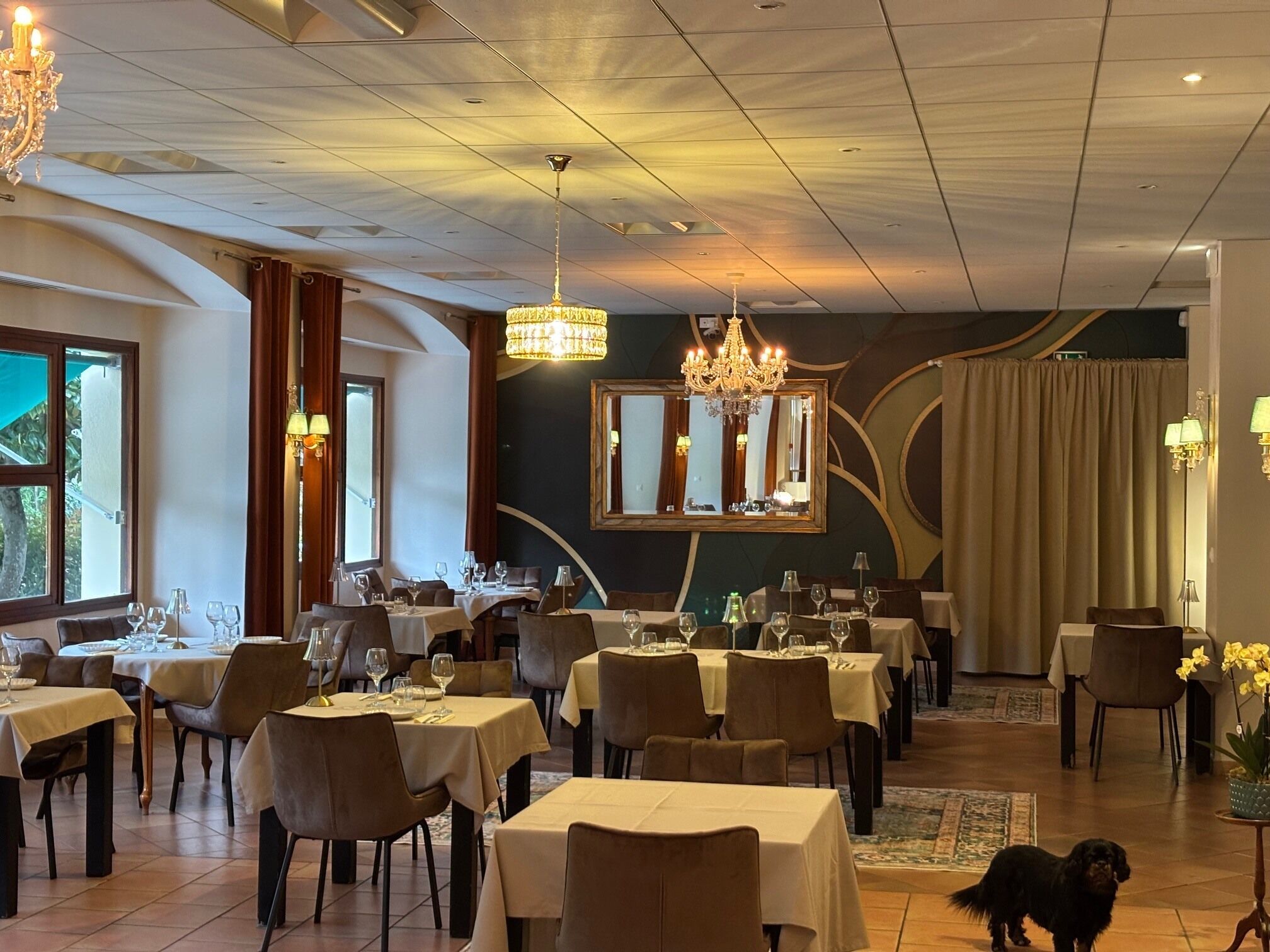 A restaurant with multiple tables, chairs, chandeliers, and a large mirror.