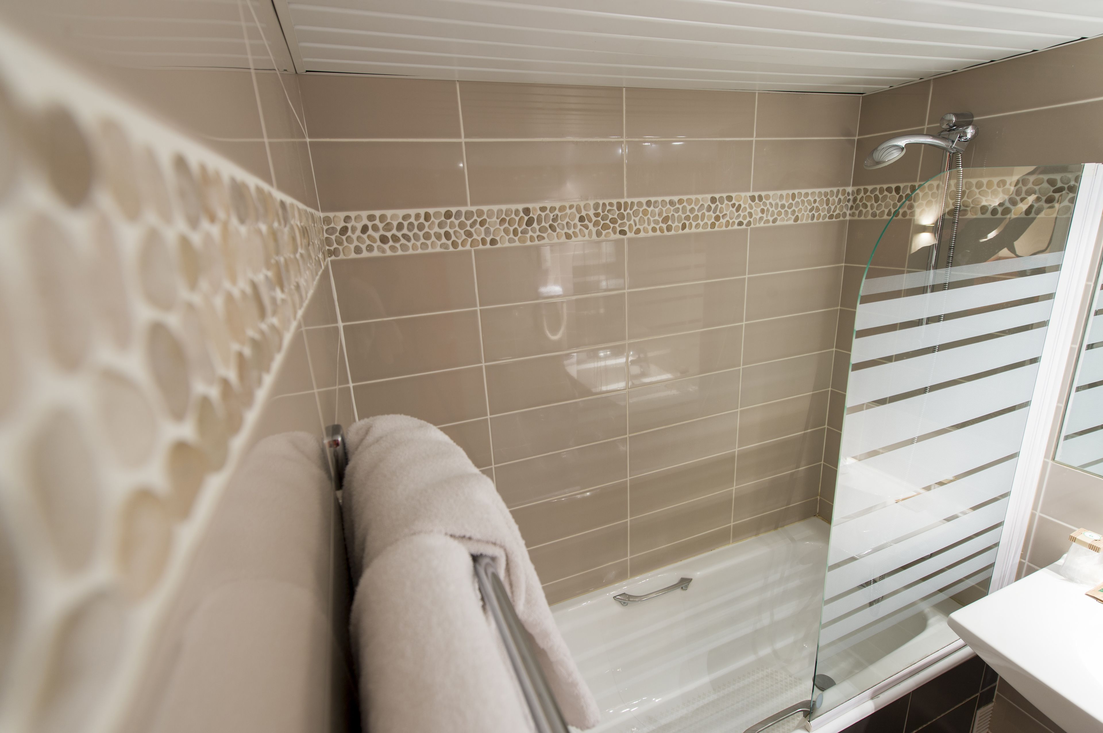 Een badkamer met beige betegelde wanden, een glazen douchecabine en een witte wastafel.