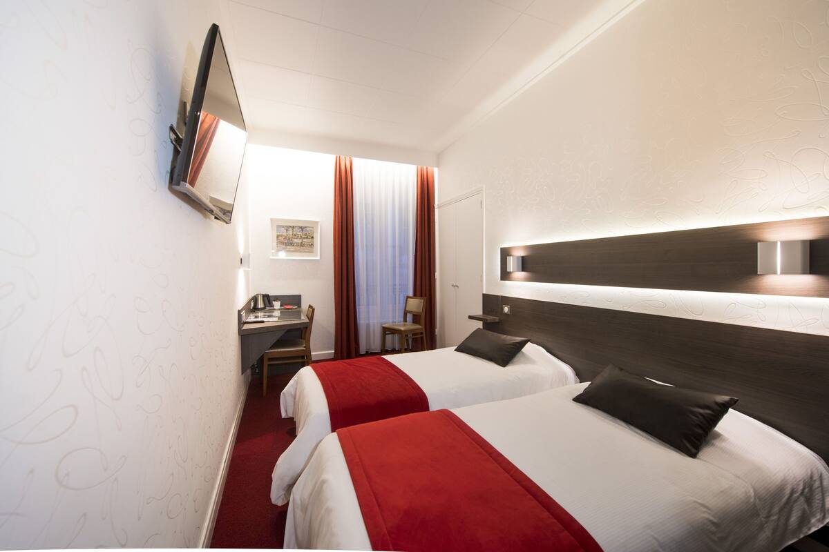 Habitación de hotel con dos camas, un escritorio, una silla y un televisor montado en la pared.