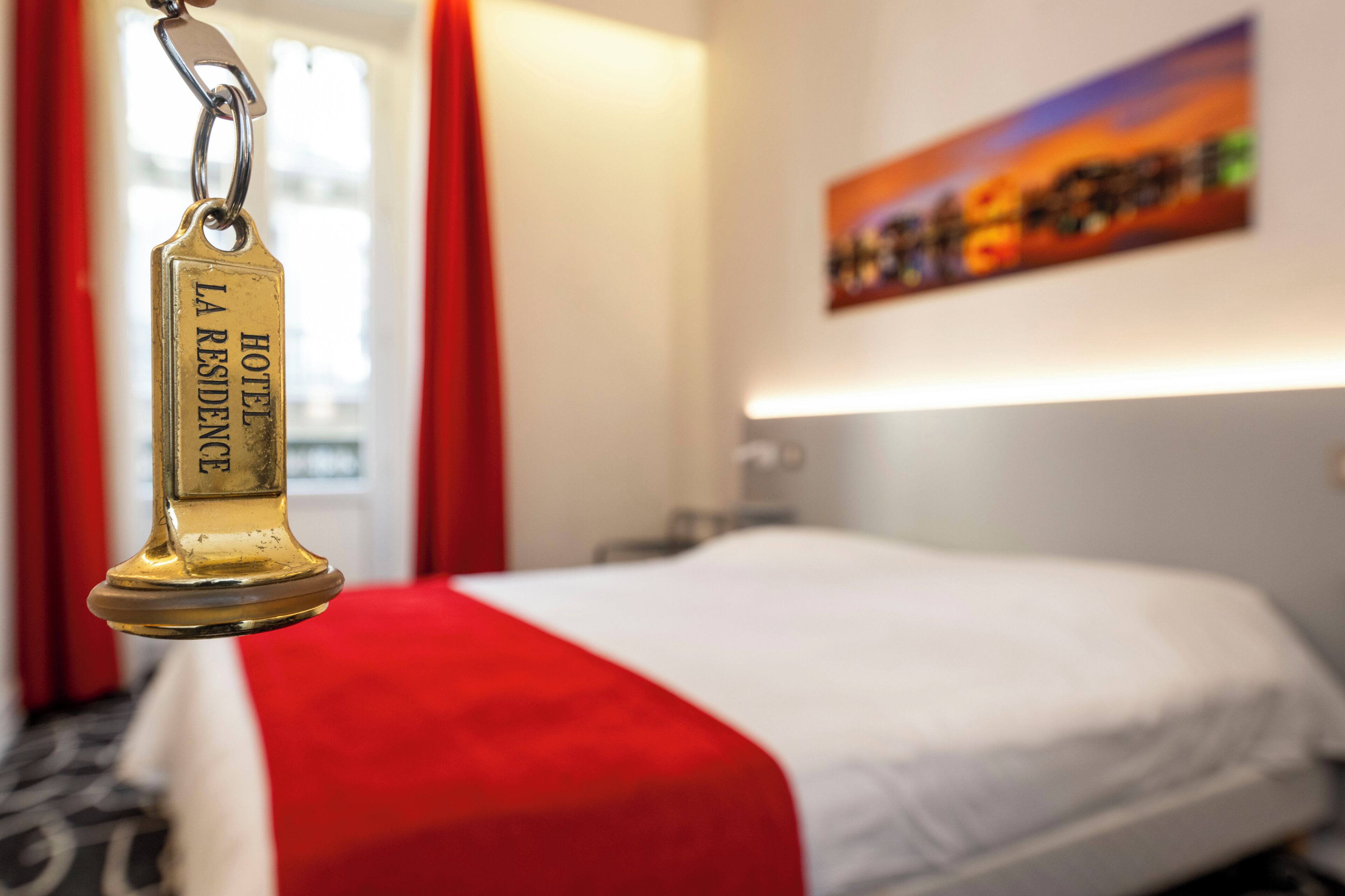 Una habitación de hotel con una cama, una cortina roja y un cuadro en la pared.