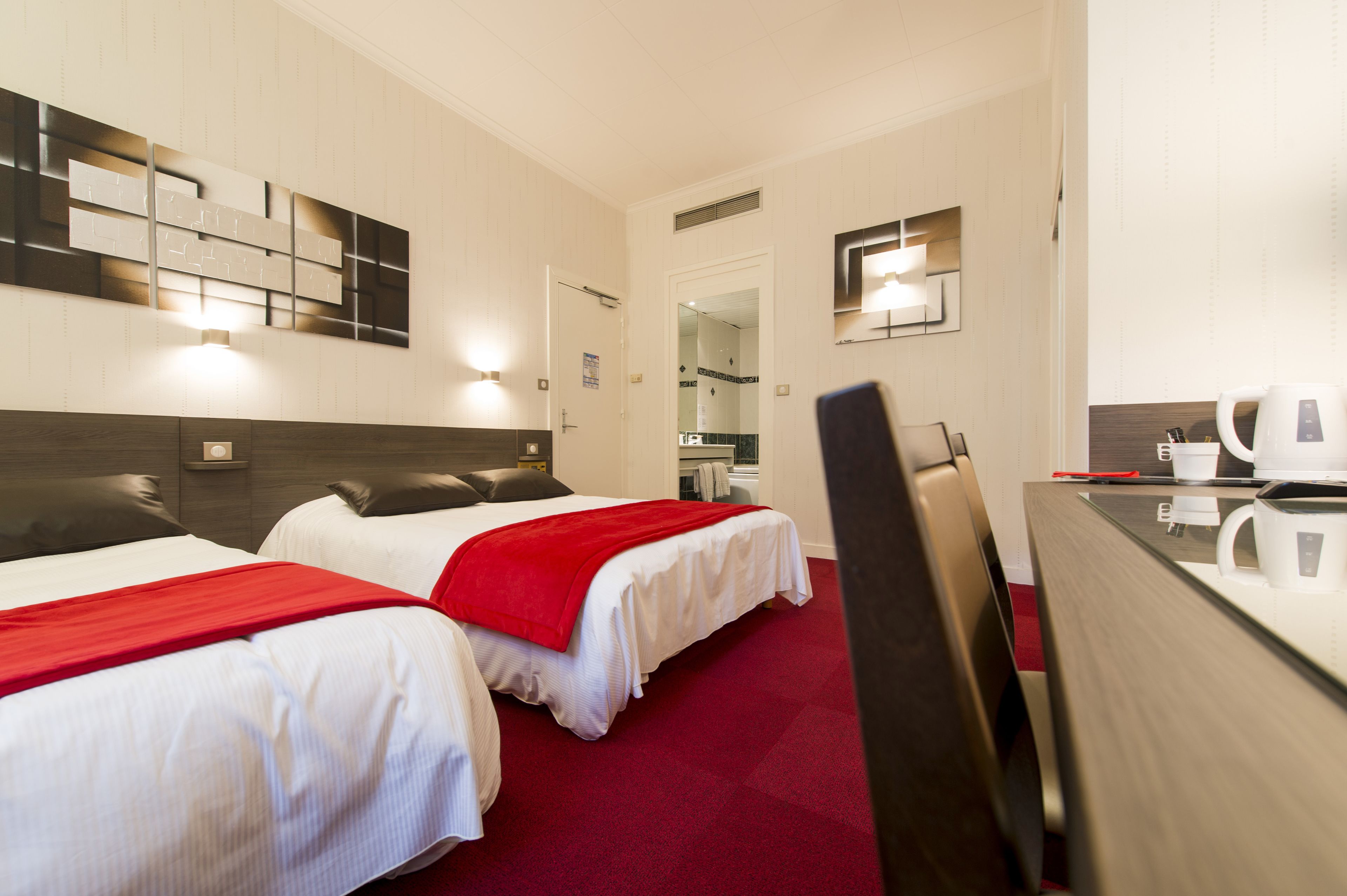 A hotel room with two beds, a desk, a mirror, and a kitchenette.