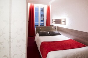 Camera d'albergo con un letto, una tenda rossa, una testiera in legno e un lampadario fissato al muro.
