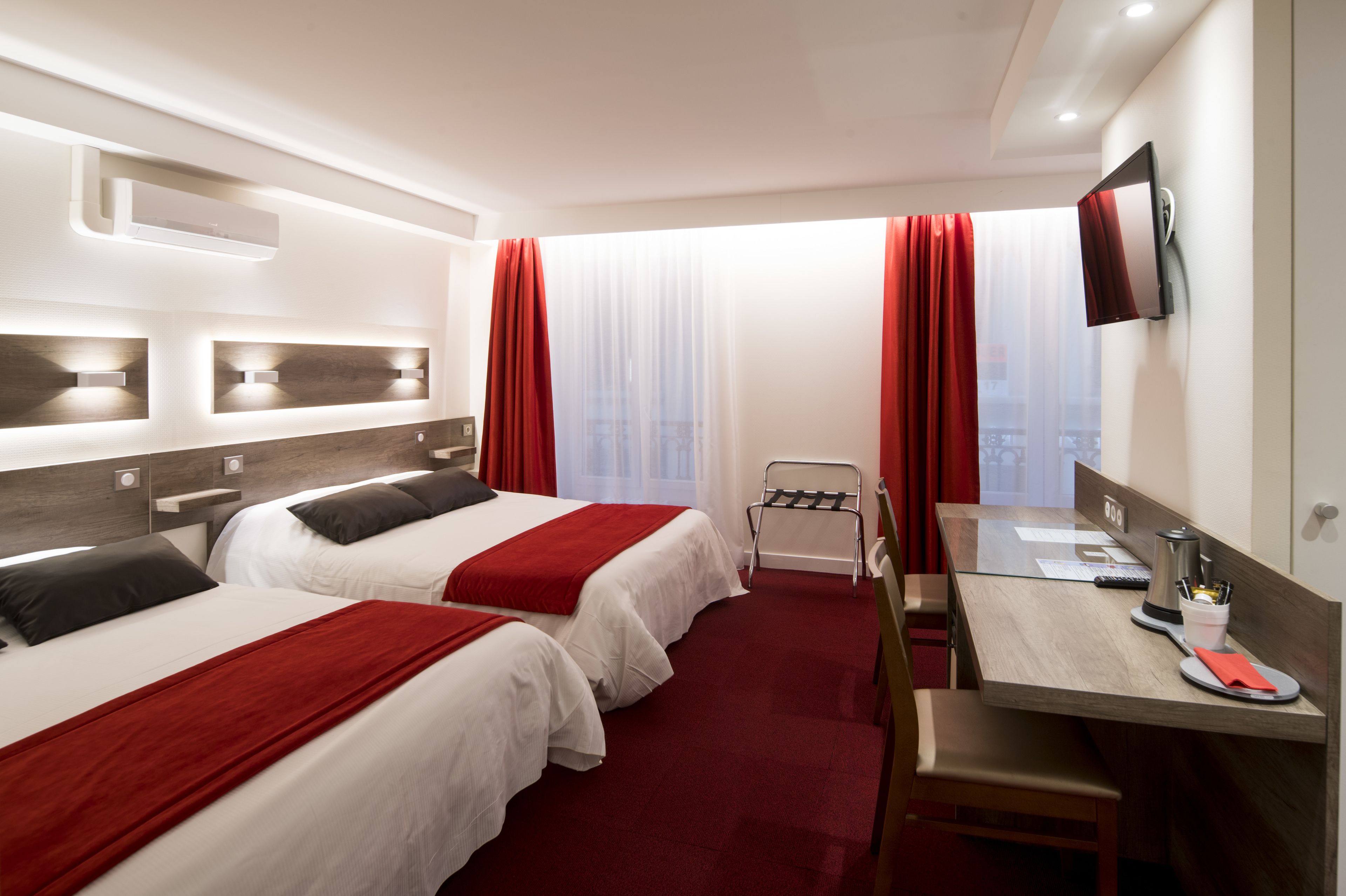 Une chambre d’hôtel avec deux lits, un bureau, une chaise, une télévision et une fenêtre avec des rideaux.