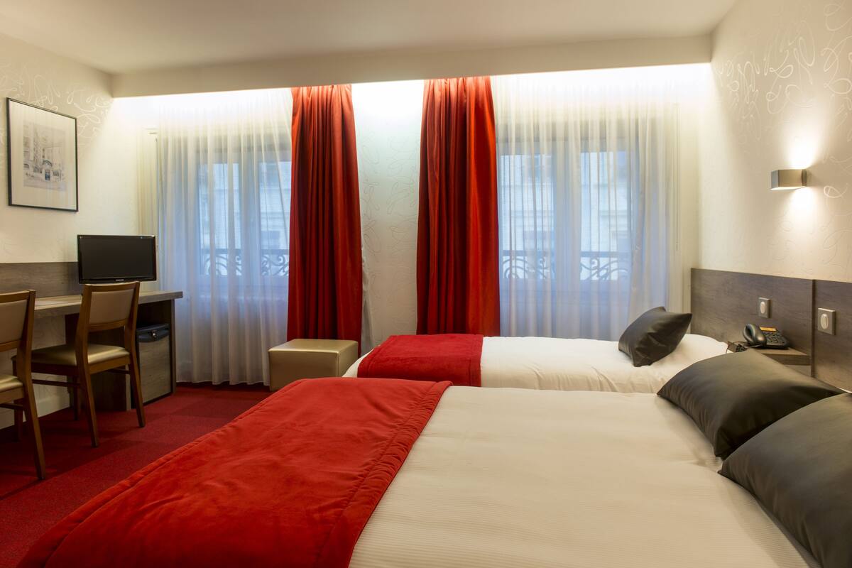 Habitación de hotel con dos camas, un escritorio, una silla y un televisor.