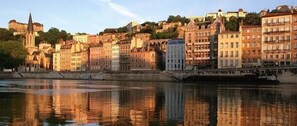 Une vue urbaine le long d’une rivière, avec des bâtiments historiques et une église imposante.