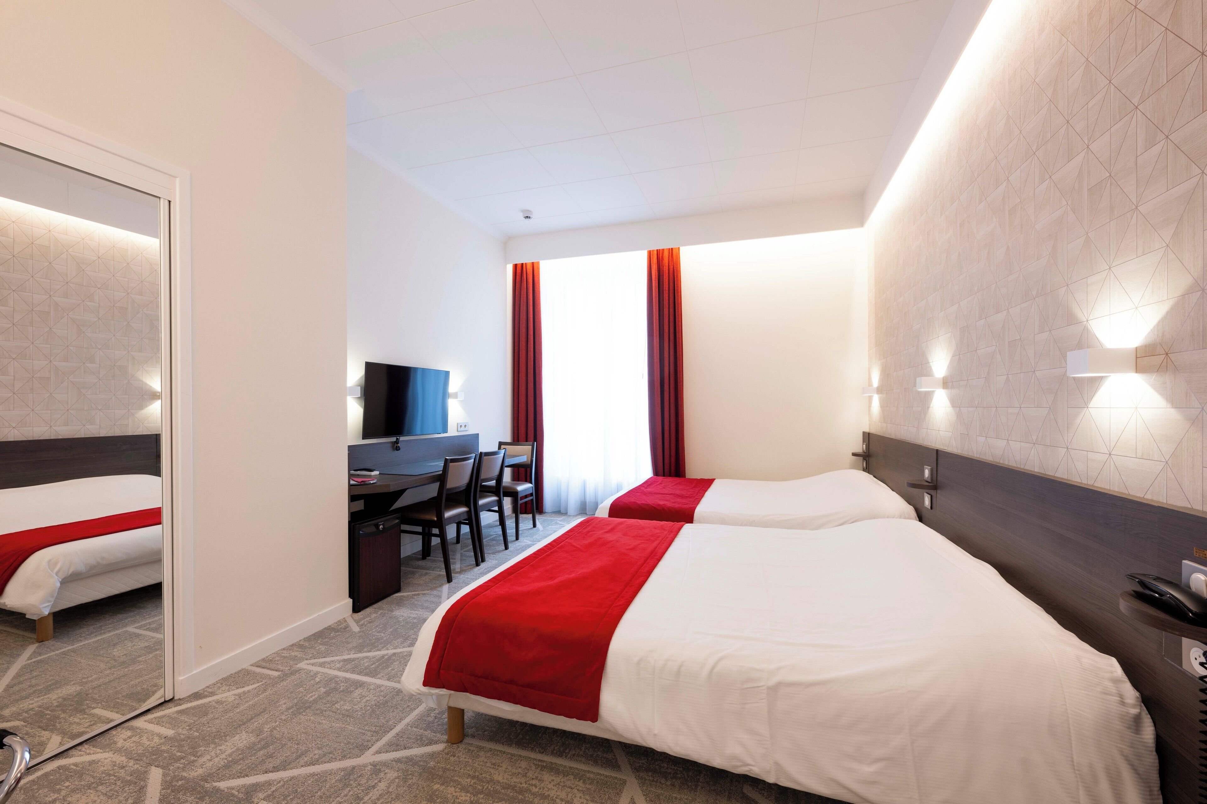Une chambre d’hôtel avec deux lits, un bureau et une télévision.