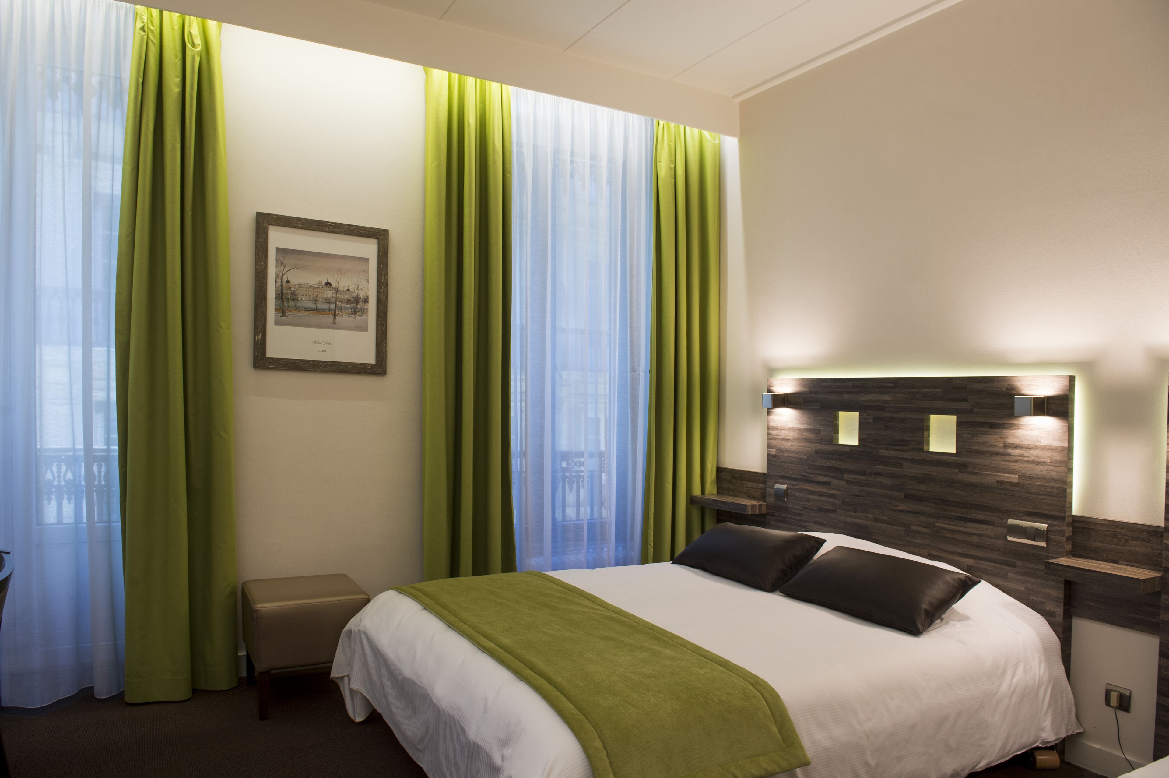 A hotel room with a bed, green curtains, a framed picture on the wall, and a nightstand with a lamp.