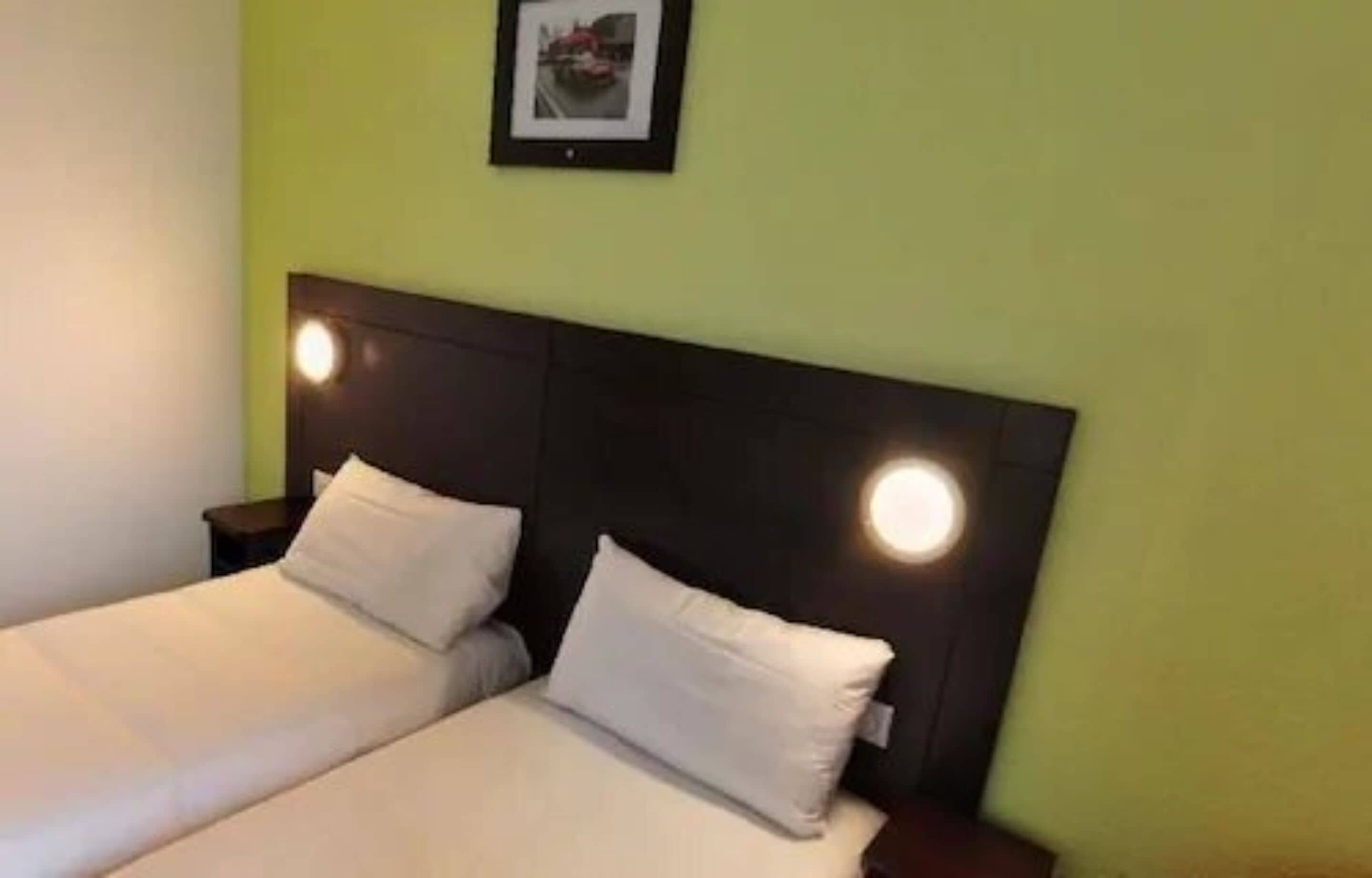 A double bed with white bedding and a dark headboard, two bedside tables, and a framed picture on the wall.