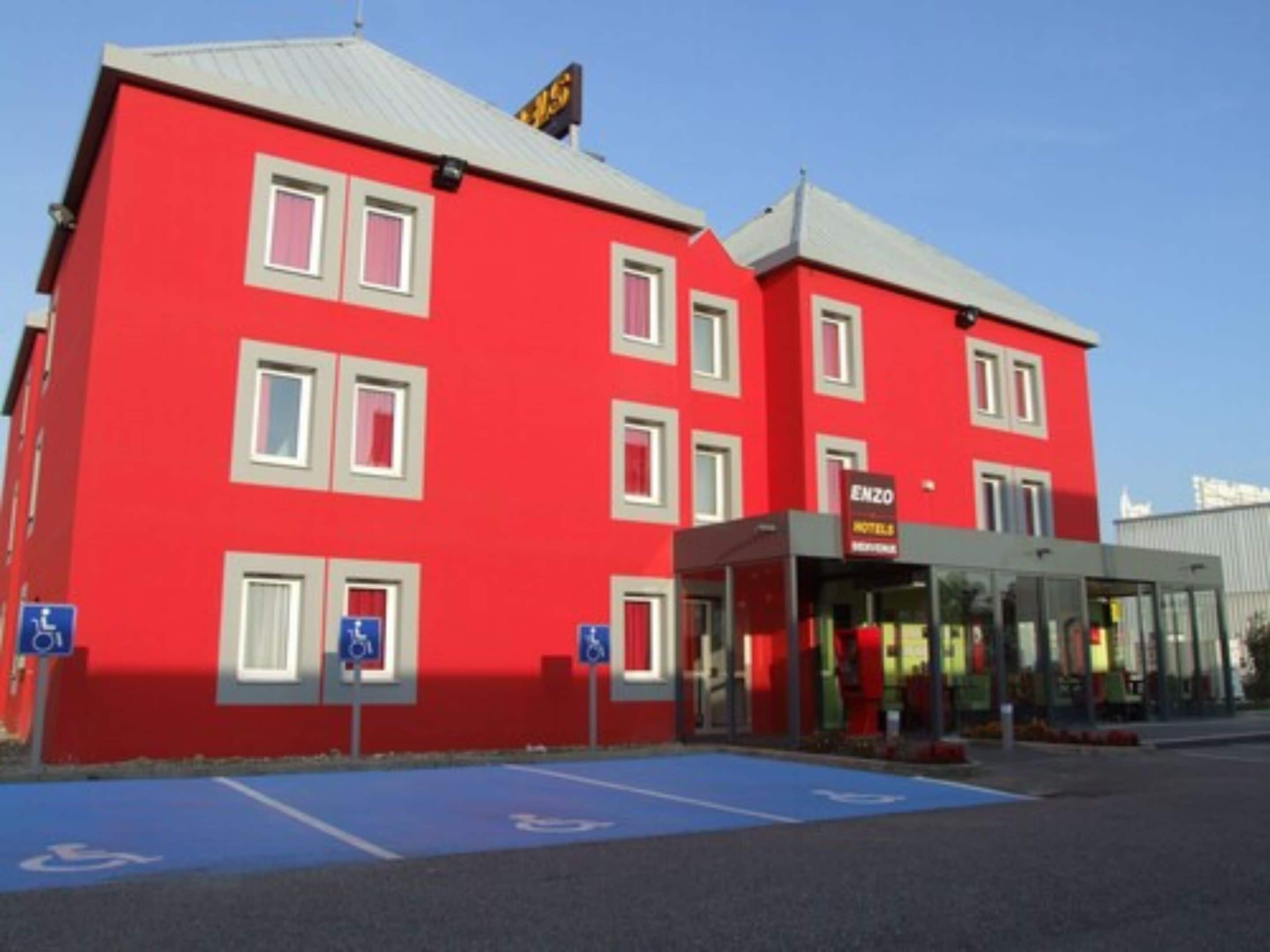 Un hotel rosso con posti auto accessibili e un cartello con la scritta Enzo Hotel.