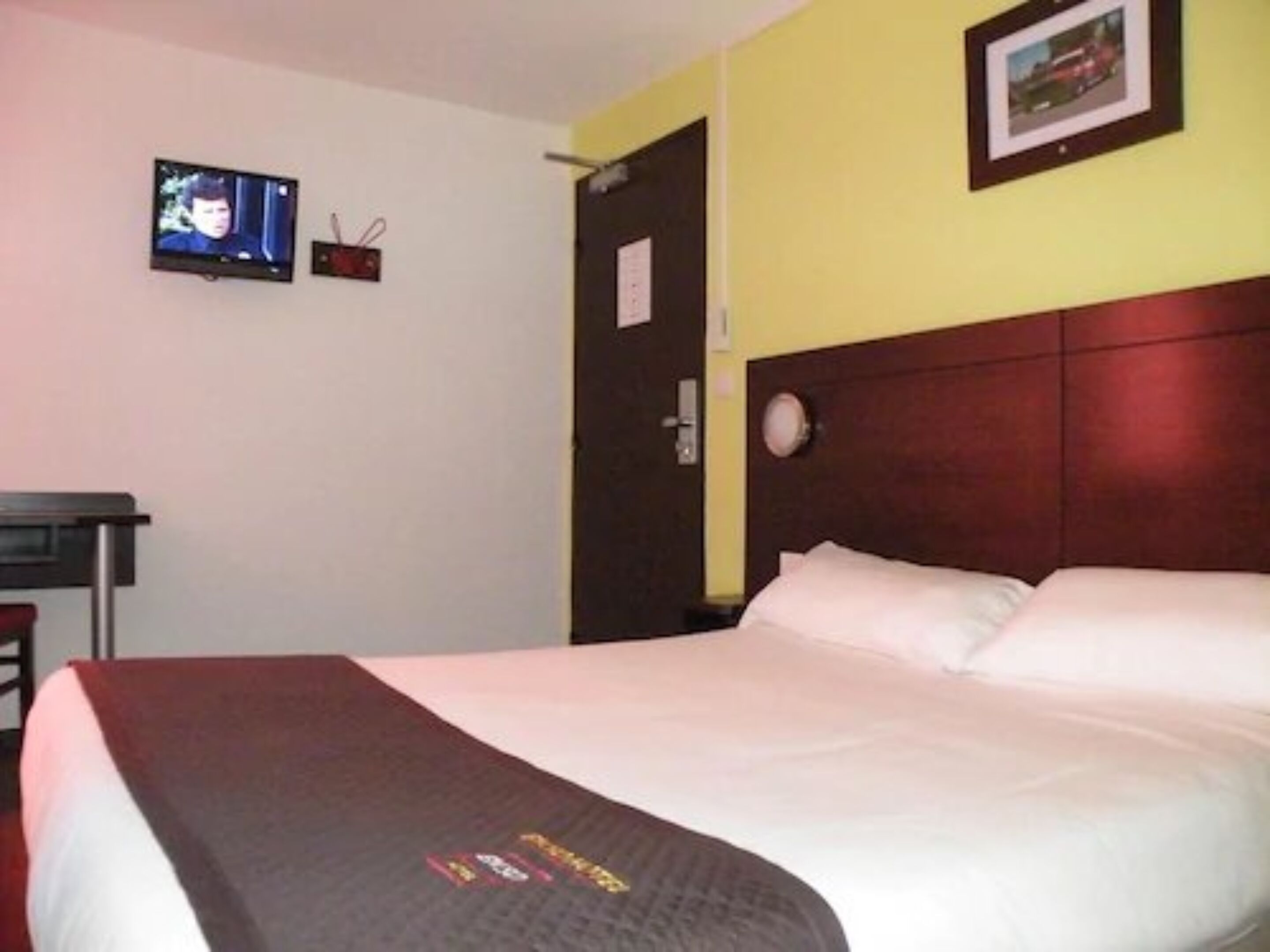 A hotel room with a bed, a television on the wall, and a door.