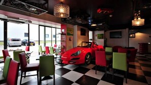 A car showroom with a red convertible on display, checkered flooring, and colorful chairs. - Enzo Hotels Mulhouse Sud Morschwiller (Morschwiller-le-Bas)
