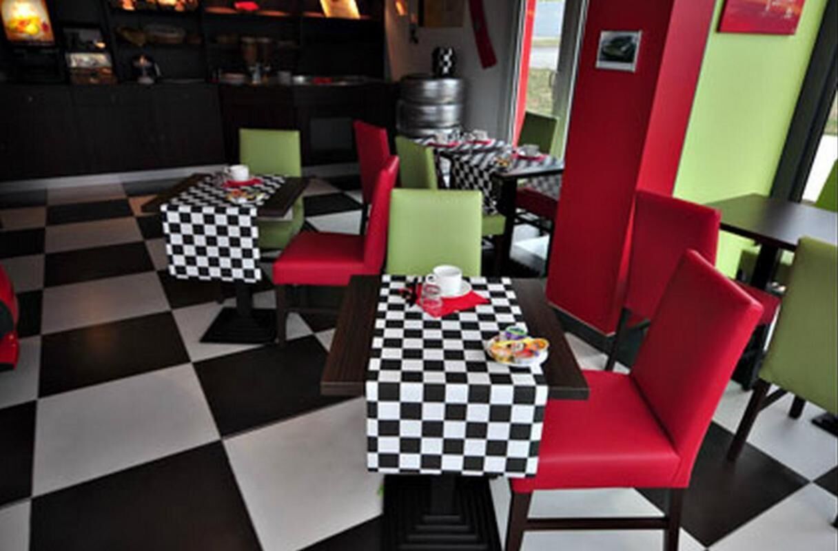 A restaurant with checkered tablecloths, red and green chairs, and a black and white floor pattern.