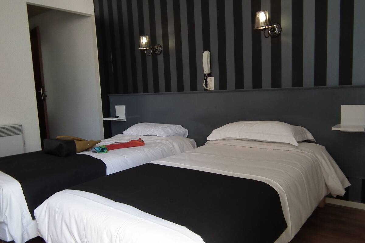 A hotel room with two beds, a bedside telephone, and a wall-mounted light fixture.