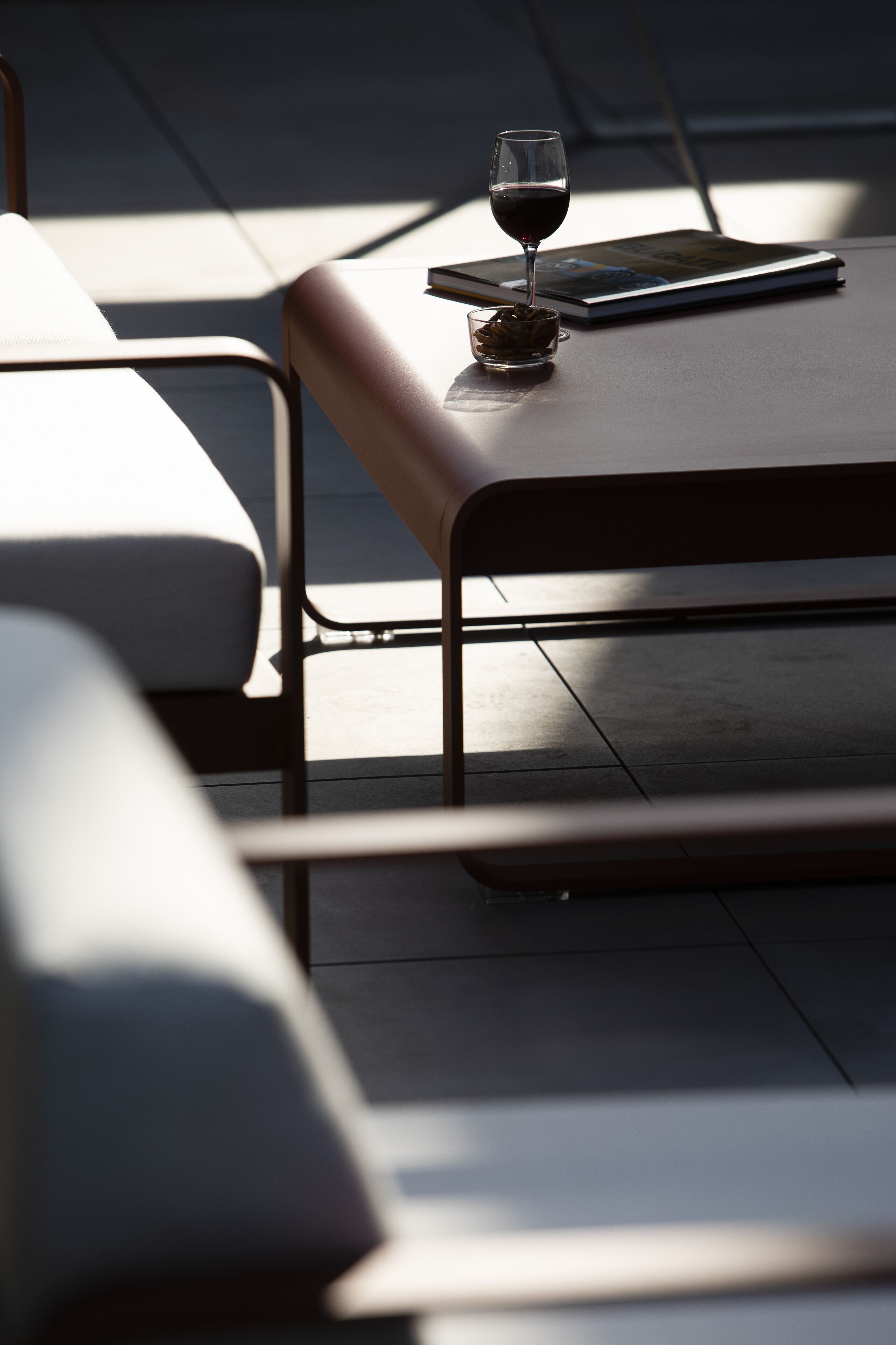 A modern outdoor seating area with a table and chairs, a glass of red wine, and a book.
