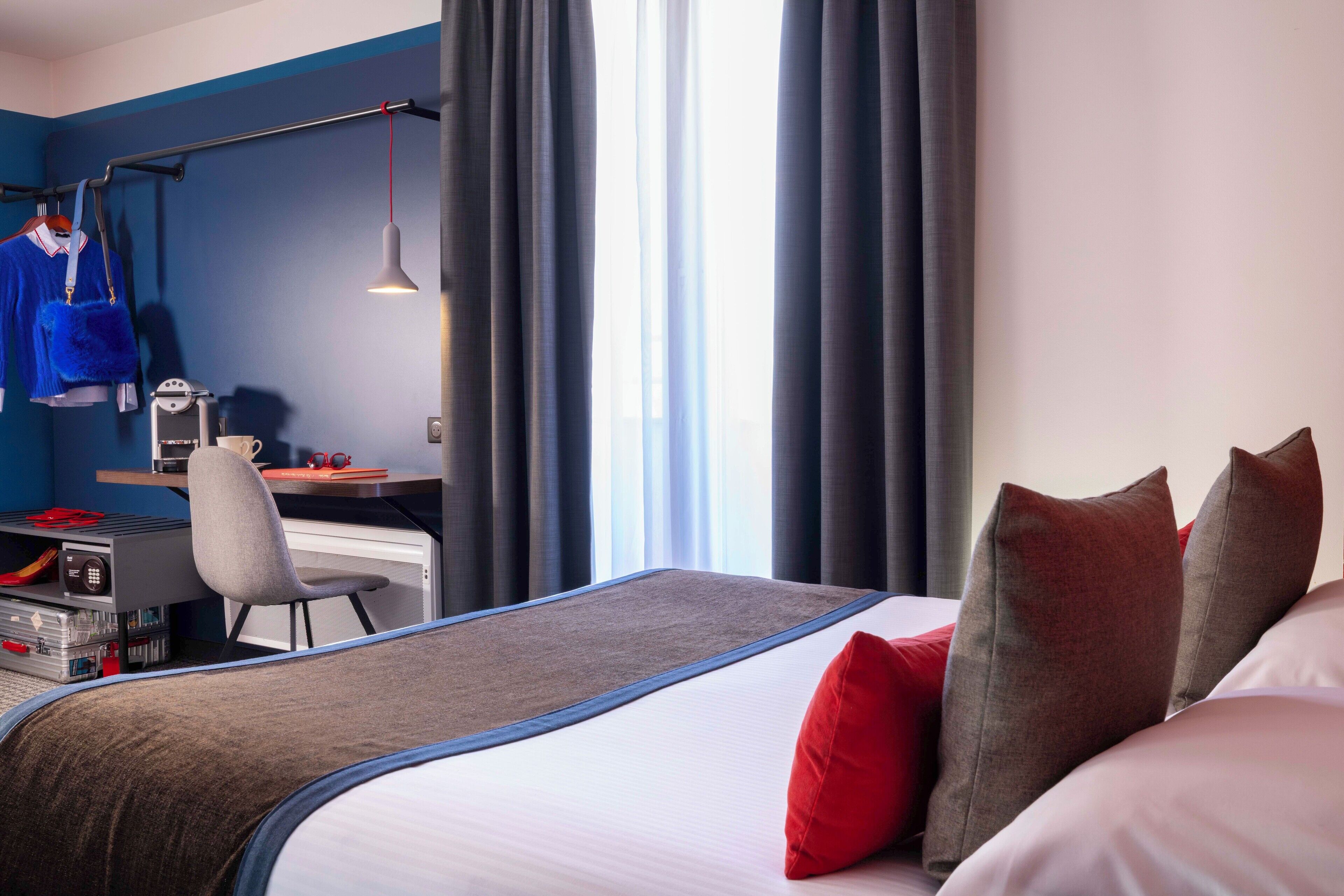 Une chambre d’hôtel avec un lit, un bureau, une chaise et une fenêtre avec des rideaux.