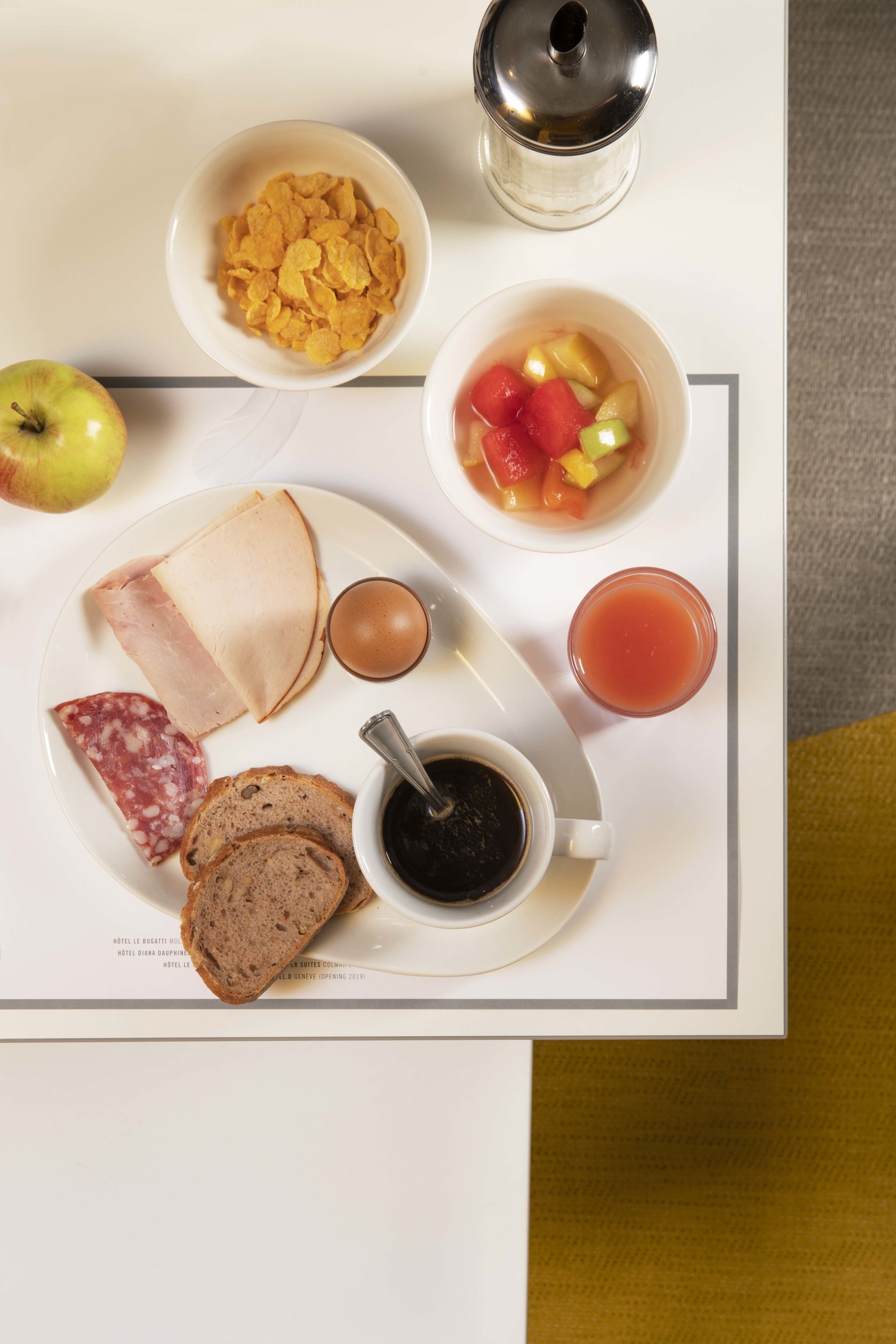 A breakfast tray with cereal, fruit, cheese, ham, bread, and a drink.