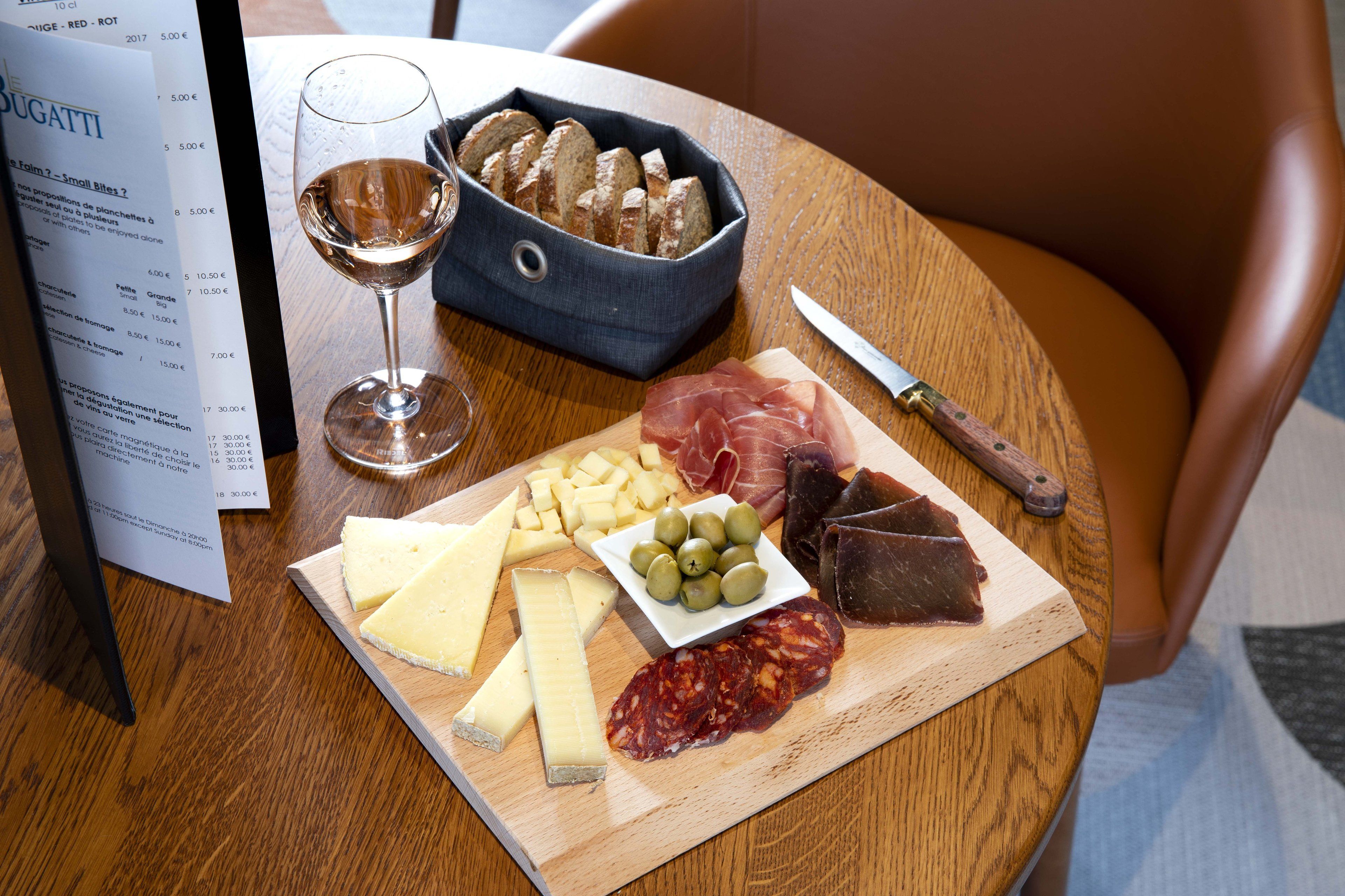 A wooden table with a cheese board, a bottle of wine, and a menu.