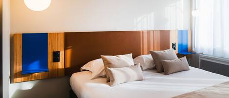 Een net opgemaakt bed met een houten hoofdbord, een blauw accentpaneel en een grote ronde lamp erboven.