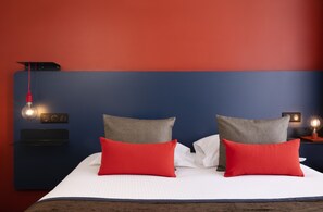 A bed with white linens, two red pillows, and a blue headboard. - Hôtel Le Bugatti (Molsheim)