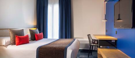 A hotel room with a large bed, a desk, a chair, a TV, and a window with curtains.