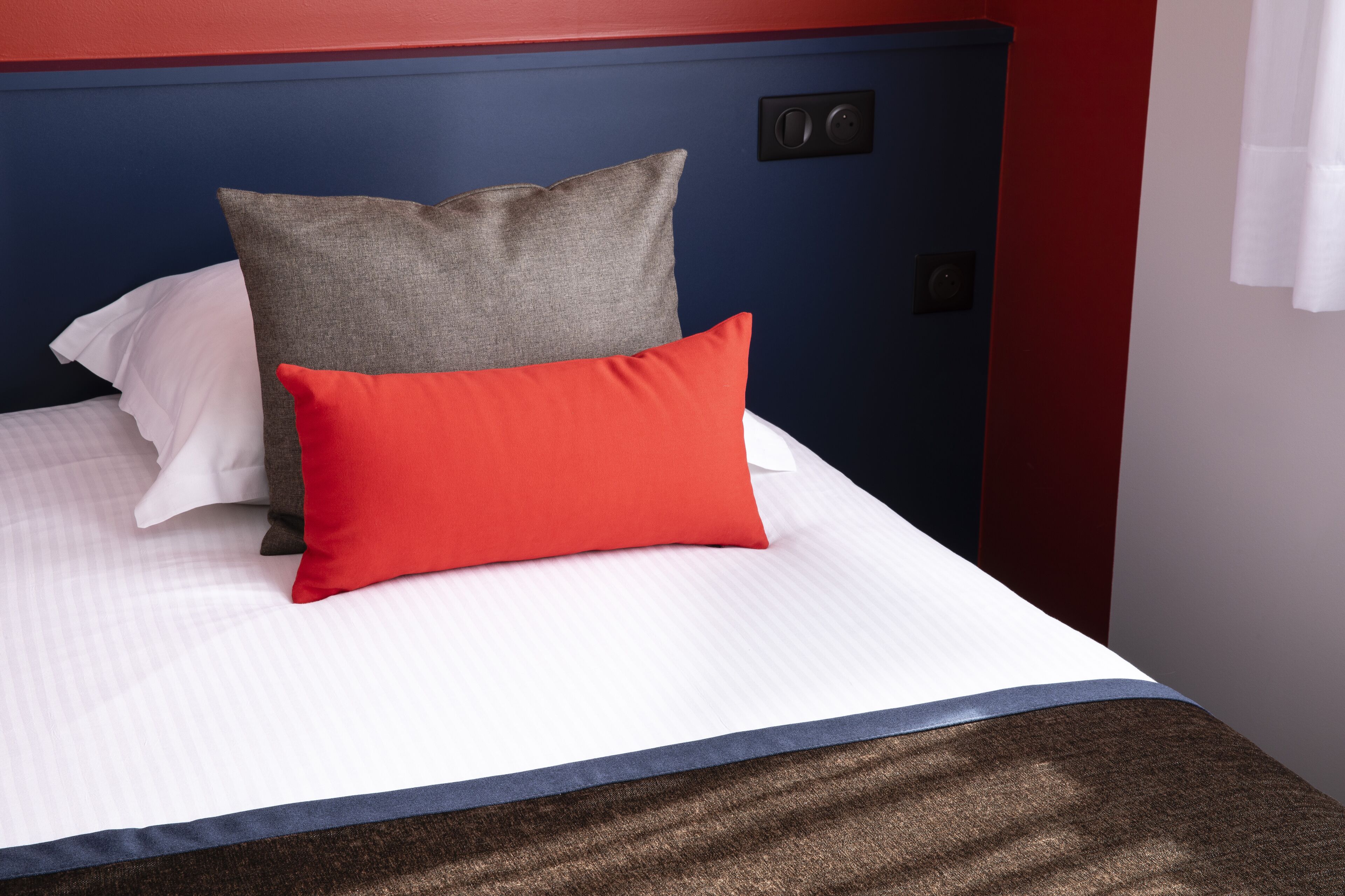 A bed with white bedding, a red pillow, and a grey pillow.