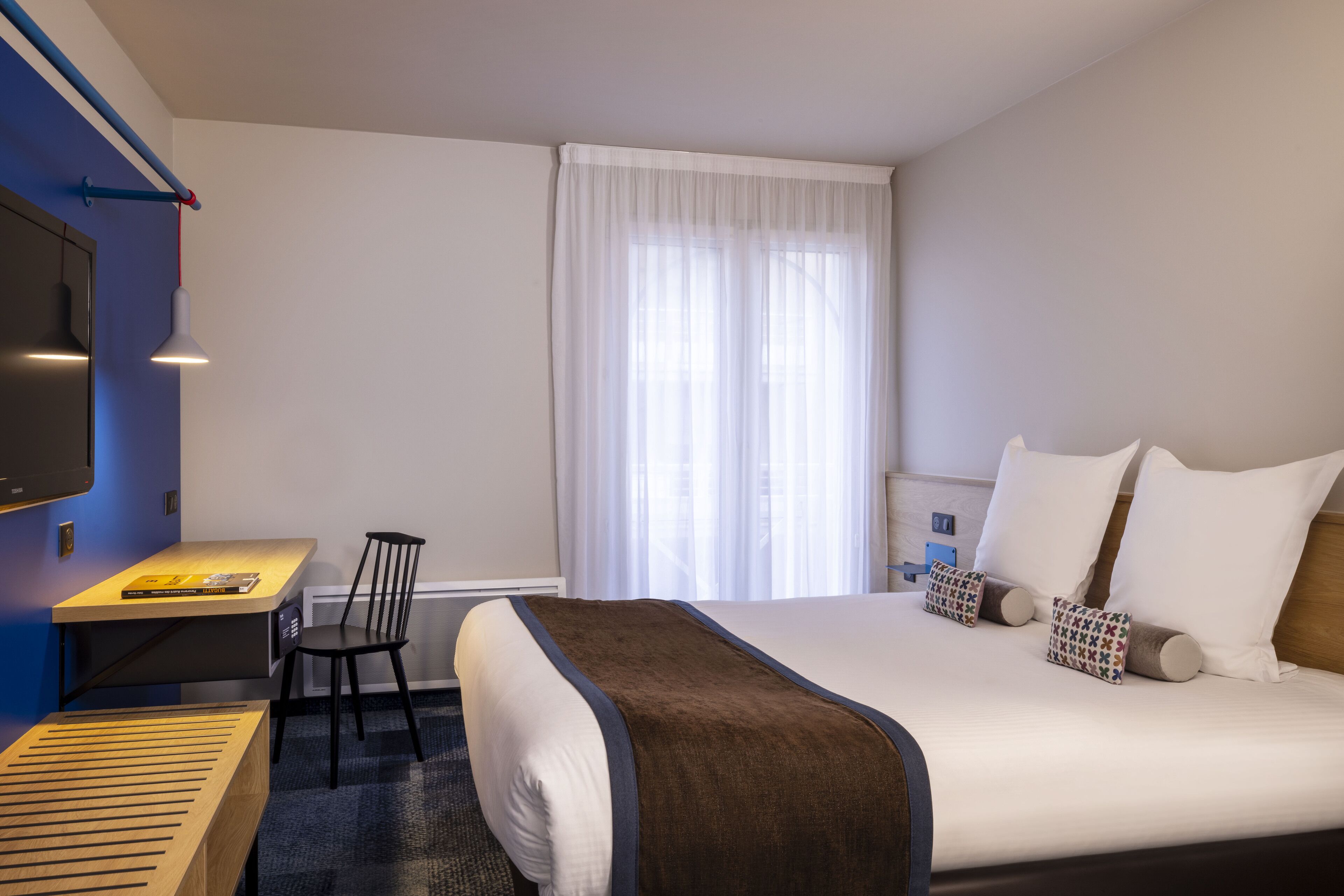 Ein Hotelzimmer mit Bett, Schreibtisch, Stuhl und Fernseher.