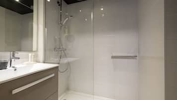 Een moderne badkamer met een douche met glazen wand, een witte wastafel en een spiegel.