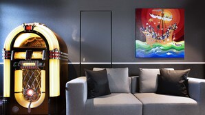 A modern living room with a vintage jukebox, a grey sofa with black cushions, and a colorful abstract painting on the wall. - Hôtel Le Bugatti (Molsheim)