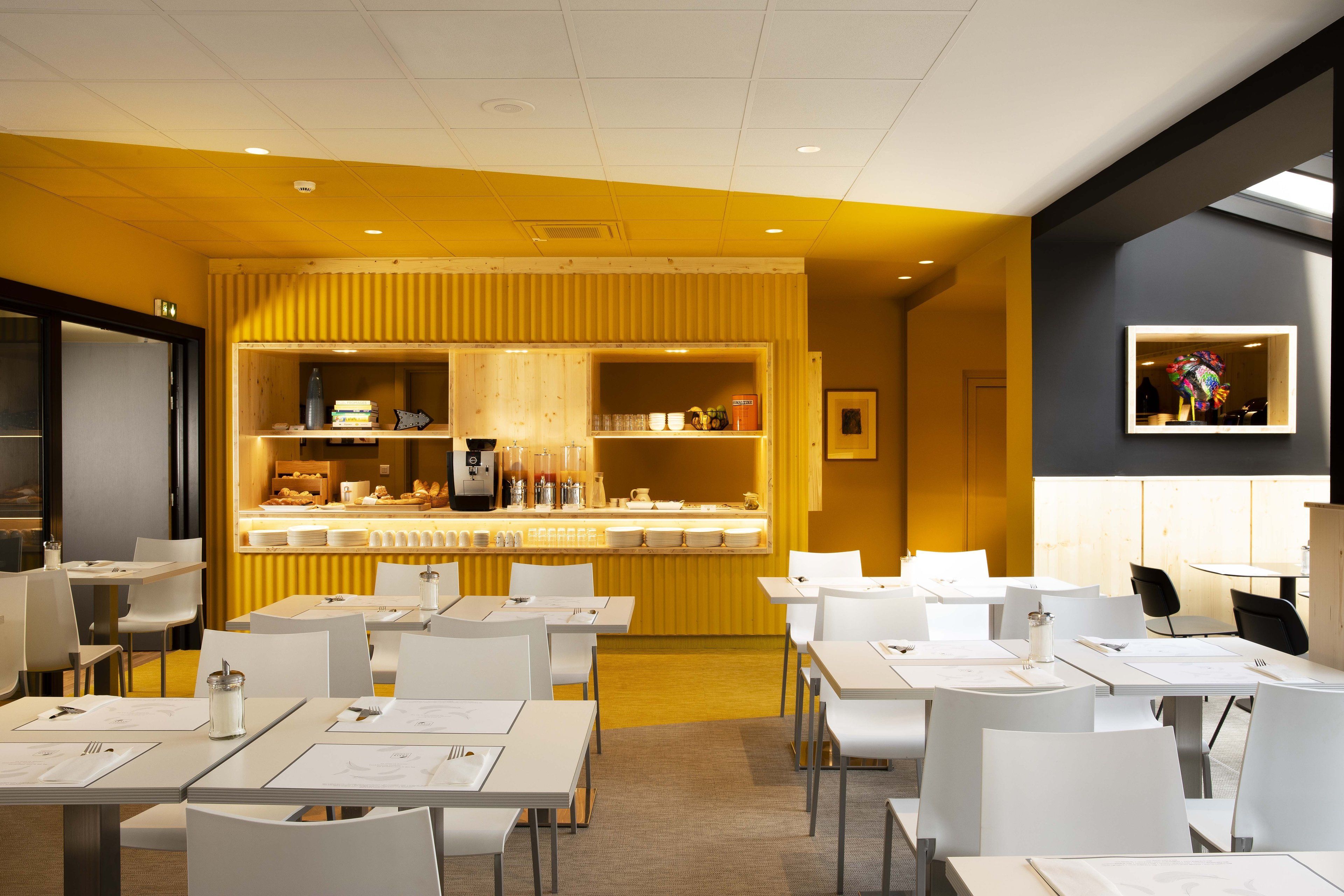 A modern dining area with white tables and chairs, a central counter with food items, and a framed picture on the wall.