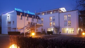 A hotel with a modern facade, multiple balconies, and a prominent illuminated sign. - Hôtel Le Bugatti (Molsheim)