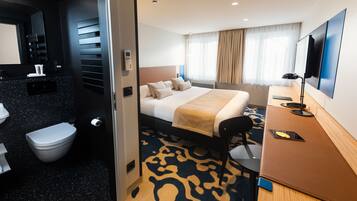 Habitació d'hotel amb llit, escriptori, cadira, televisió i bany.