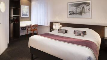 A hotel room with a large bed, a desk, and a chair.