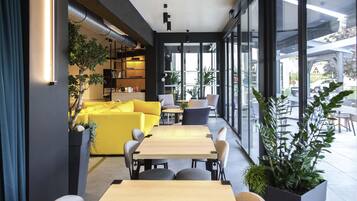 Een modern interieur met een gele bank, houten tafels en potplanten.