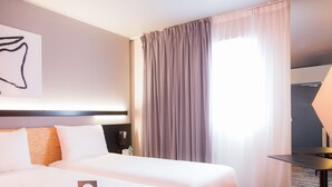 Habitación de hotel con dos camas, una mesita de noche, una lámpara y un ventanal con cortinas.