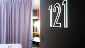 Een deur met het nummer 121, een kamer met een bed en een lamp, en een gedeeltelijk zichtbaar gordijn.