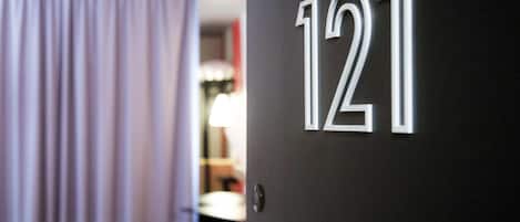 A door with the number 121, a room with a bed and a lamp, and a curtain partially visible.