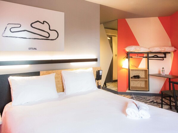 Habitación de hotel con cama, escritorio, silla, teléfono y estante con lámpara.