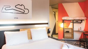 A hotel room with a bed, a desk with a chair, a phone, and a wall-mounted shelf with a lamp. - ibis Styles Bâle-Mulhouse Aéroport (Blotzheim)