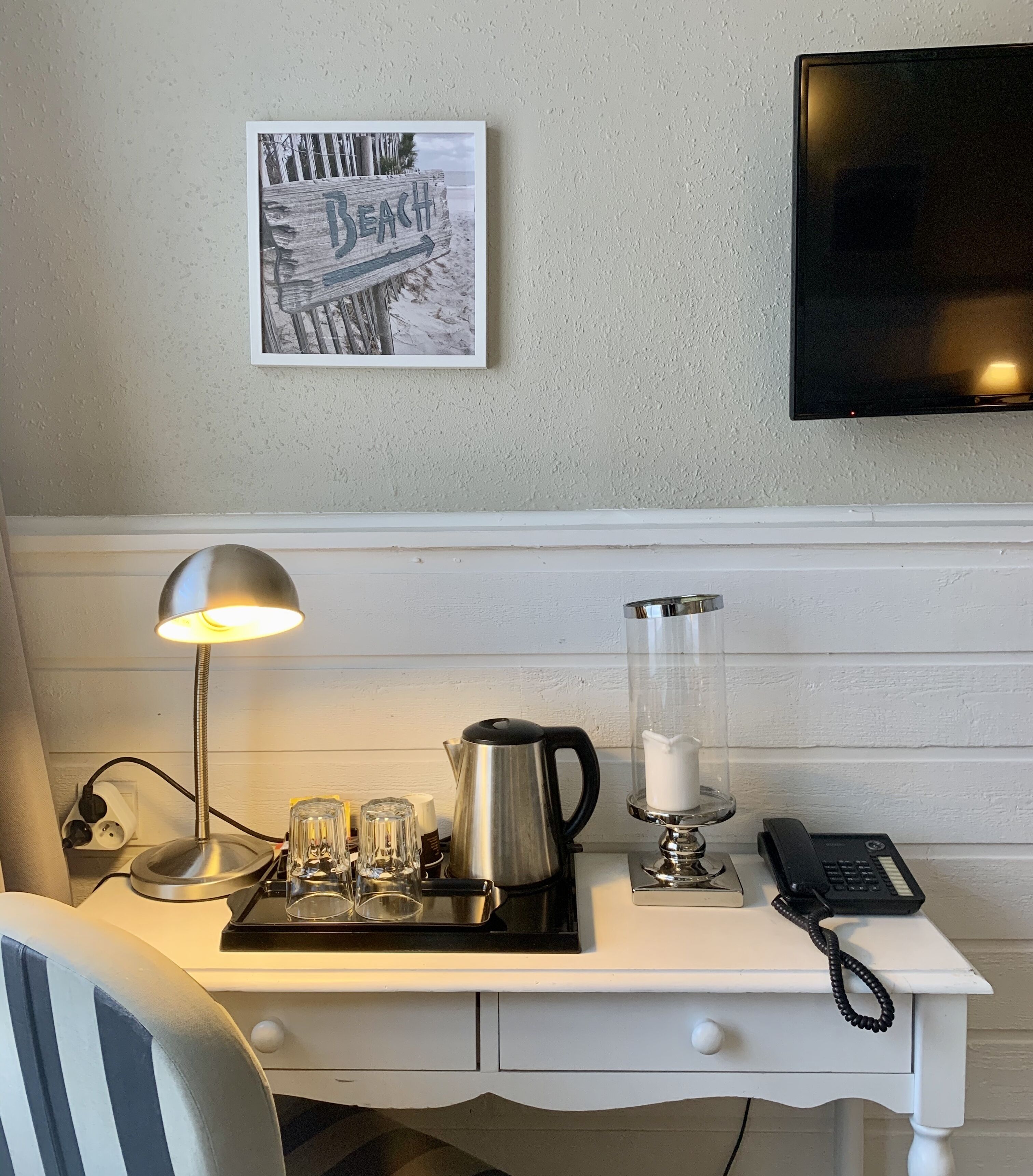 Un bureau bien rangé, avec une lampe, une cafetière, des verres, une bougie et un téléphone.