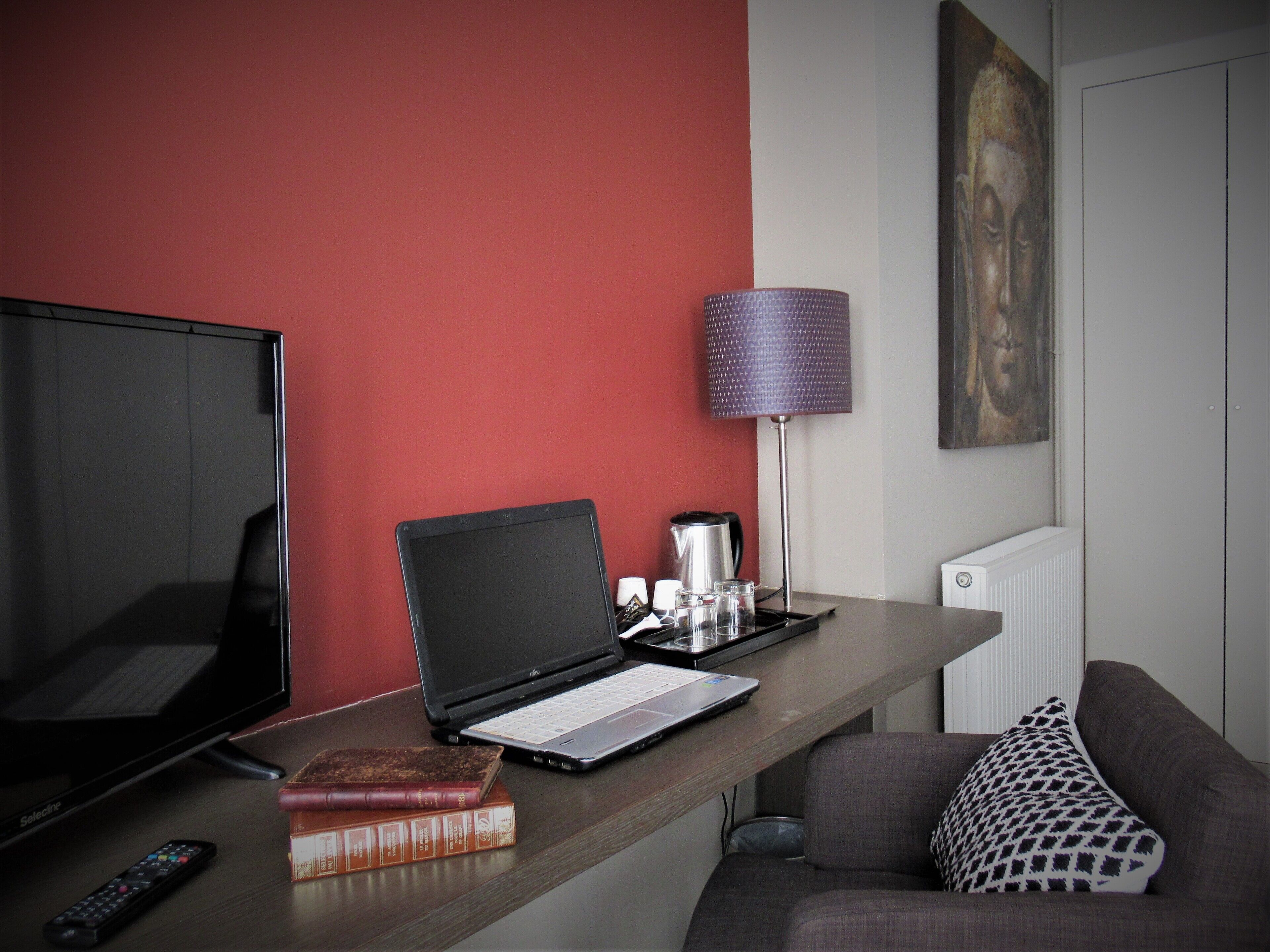 A hotel room with a desk, a laptop, a remote control, and a few books.