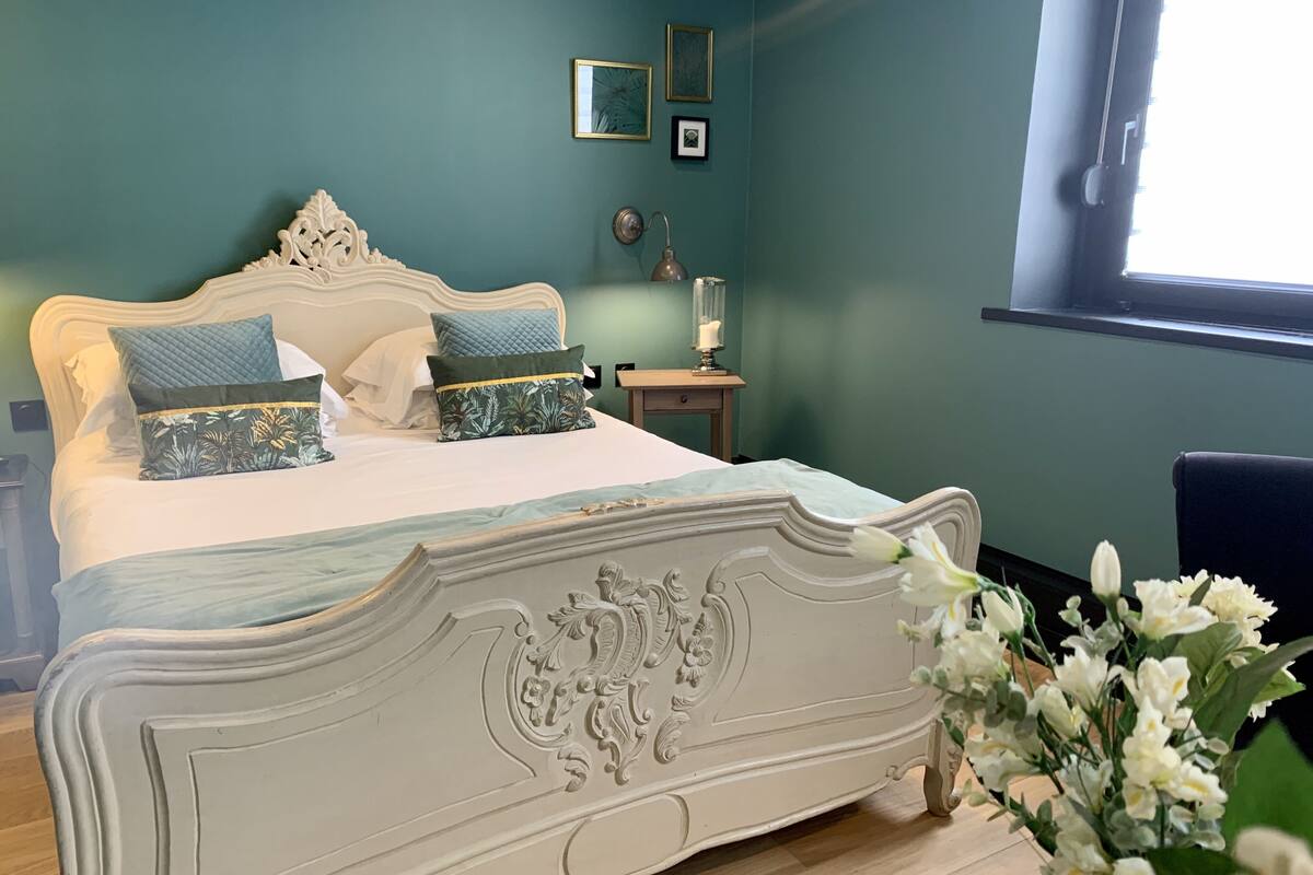 Ein Schlafzimmer mit einem großen Bett, einem Nachttisch, einer Lampe und einem Fenster.