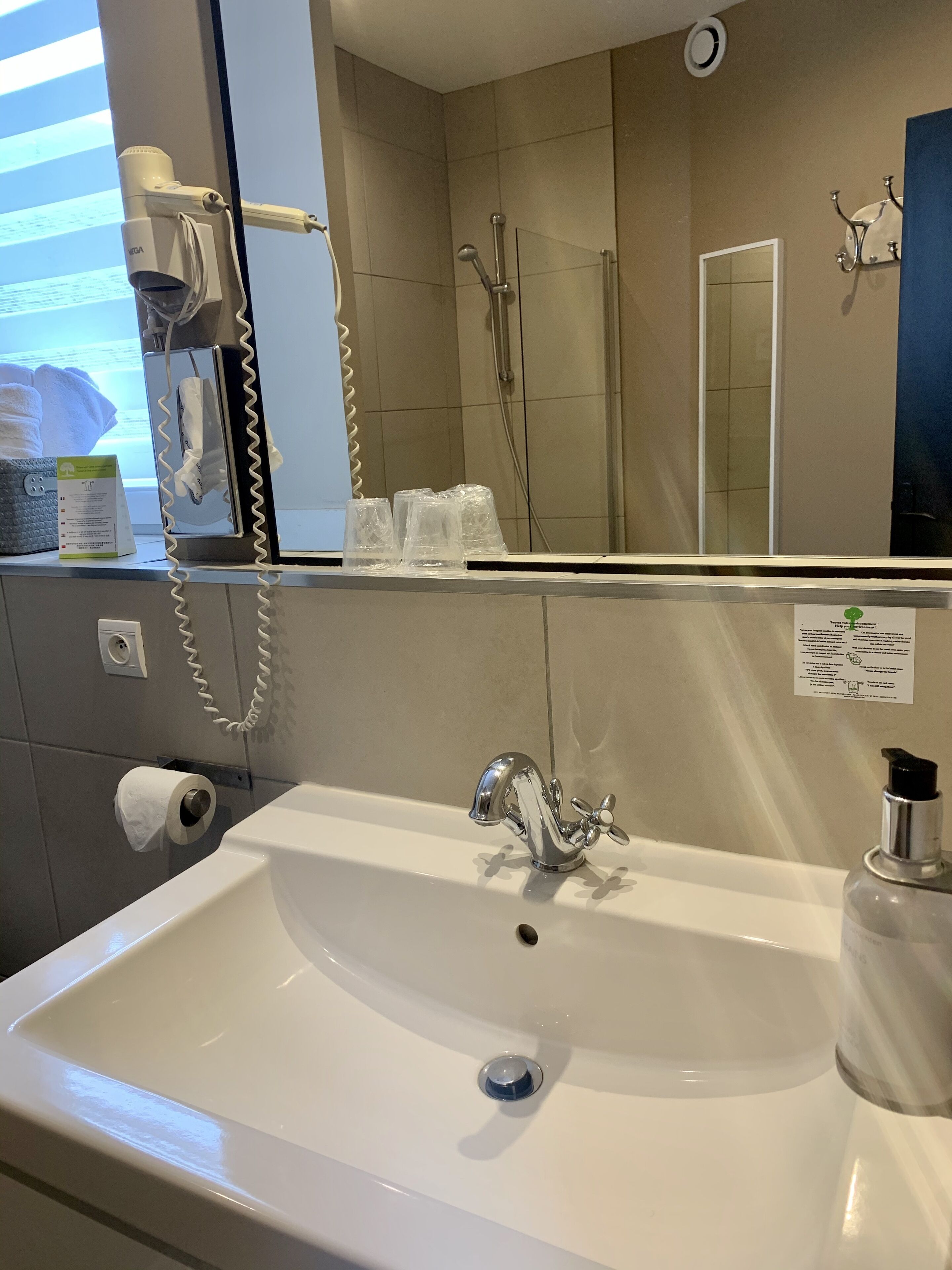 Un baño con lavamanos blanco, un espejo, dispensador de toallas y zona de ducha.