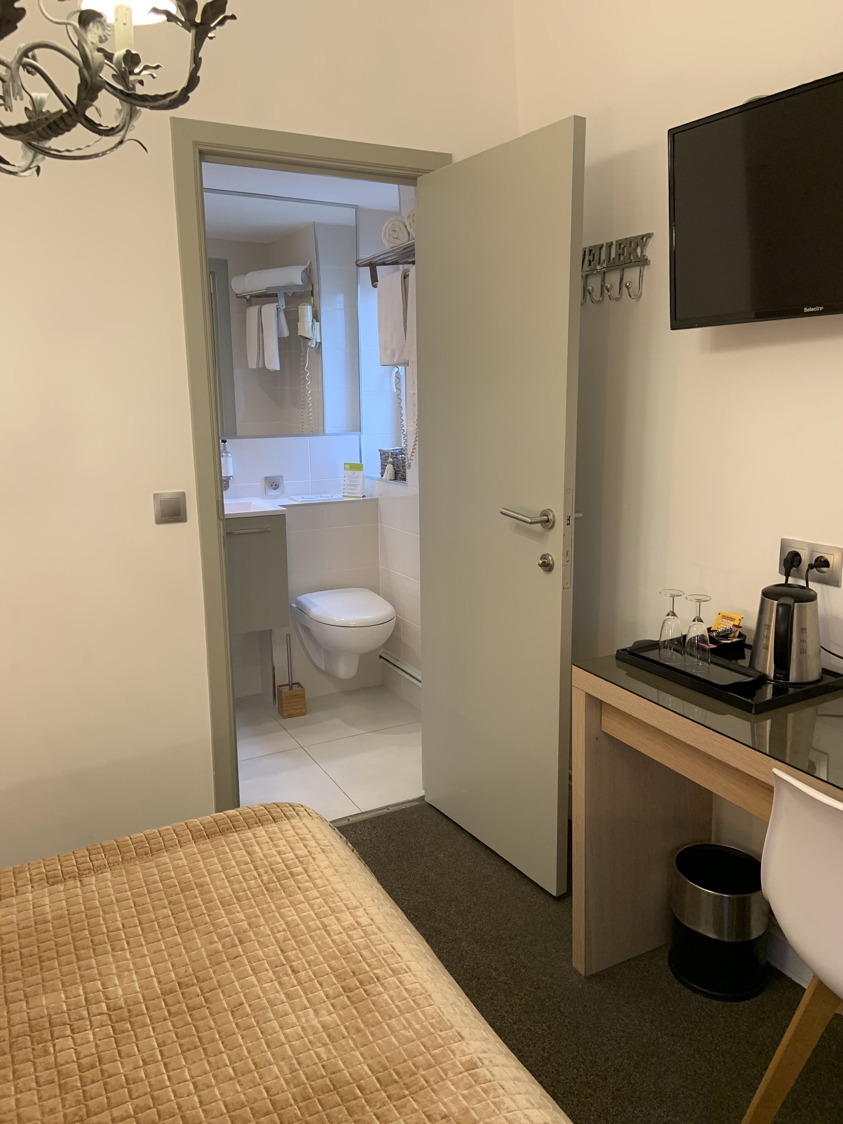 Een kleine hotelkamer met een bed, een bureau met koffiezetapparaat, een televisie en een klein prullenbakje.